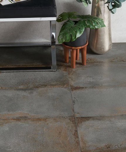 Close-up of a tiled floor with a metallic object and potted plants in the background.