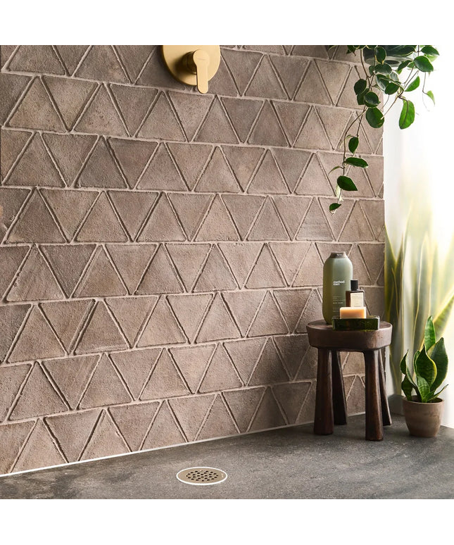 Bathroom with geometric triangle-patterned tiles, a small table with bottles, and a plant.