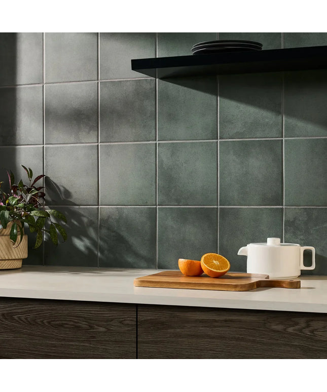 Kitchen counter with oranges on a cutting board and a white teapot against a green tiled wall.
