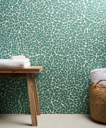 Mosaic patterned wall with wooden bench and basket containing towels.