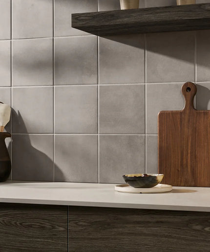 Kitchen counter with wooden cutting board, bowls, and utensils against a tiled wall.