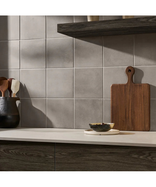 Kitchen counter with wooden cutting board, bowls, and utensils against a tiled wall.