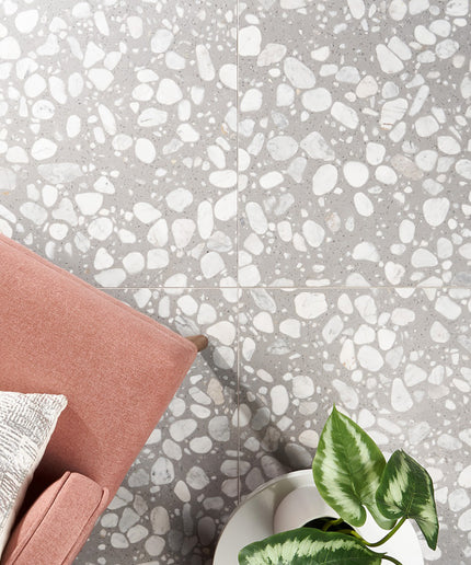 Terrazzo-style floor with gray and white pattern, pink cushion, and green plant.