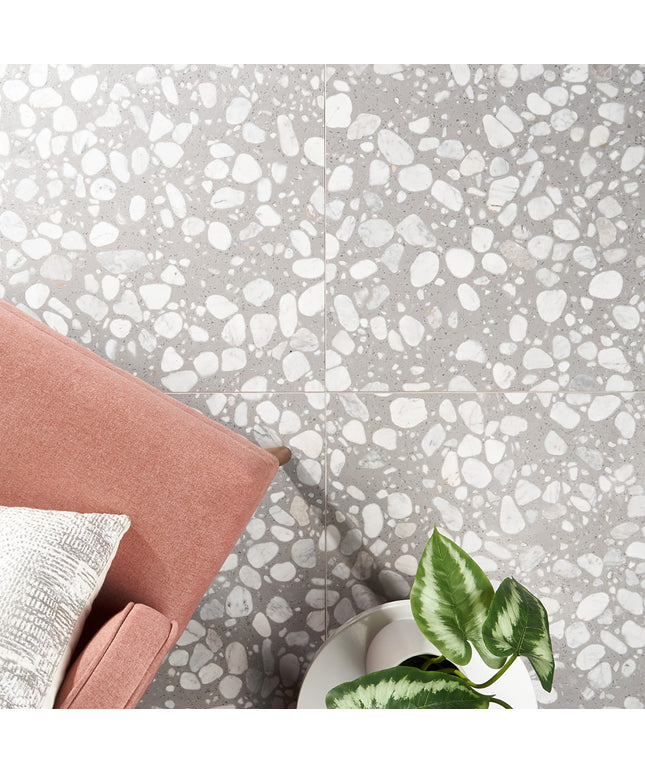 Terrazzo-style floor with gray and white pattern, pink cushion, and green plant.