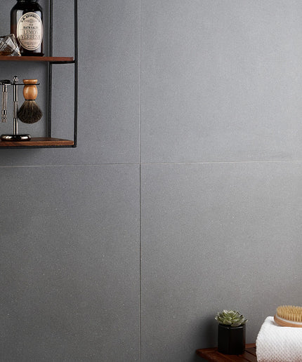 Gray tiled wall with a wooden shelf and decorative items.