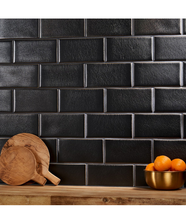 Black tiled wall with wooden cutting boards and a bowl of oranges on a wooden surface
