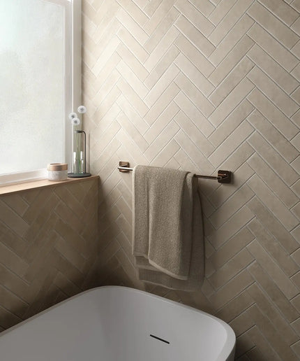 Bathroom with beige herringbone tile pattern, white bathtub, and towel rack.