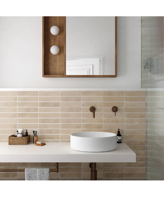 Modern bathroom with a white sink, wooden mirror, and beige tiles.