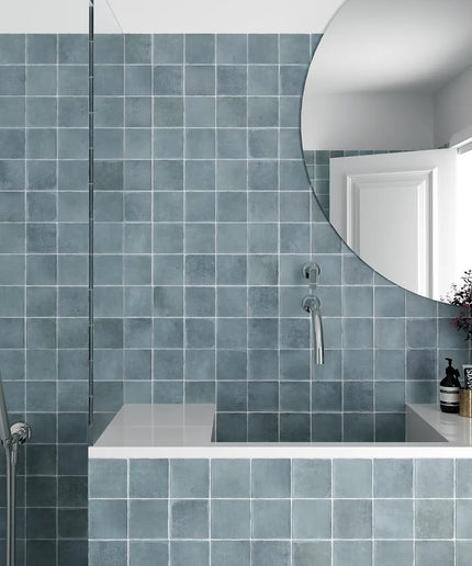 Bathroom with blue tiled walls, a round mirror, and a shower area.