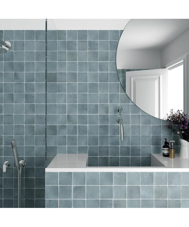 Bathroom with blue tiled walls, a round mirror, and a shower area.