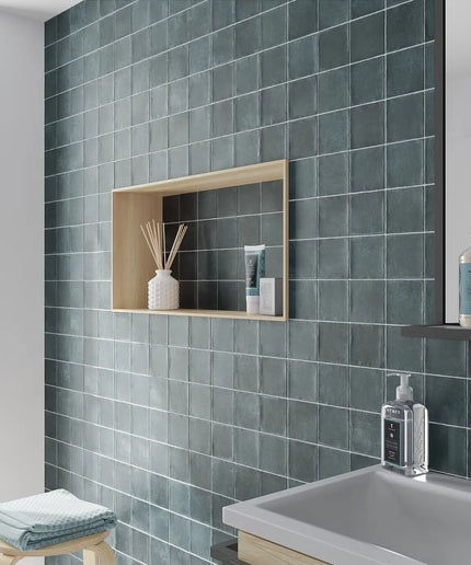 Bathroom with green tiled walls, a sink, and shelves with toiletries.