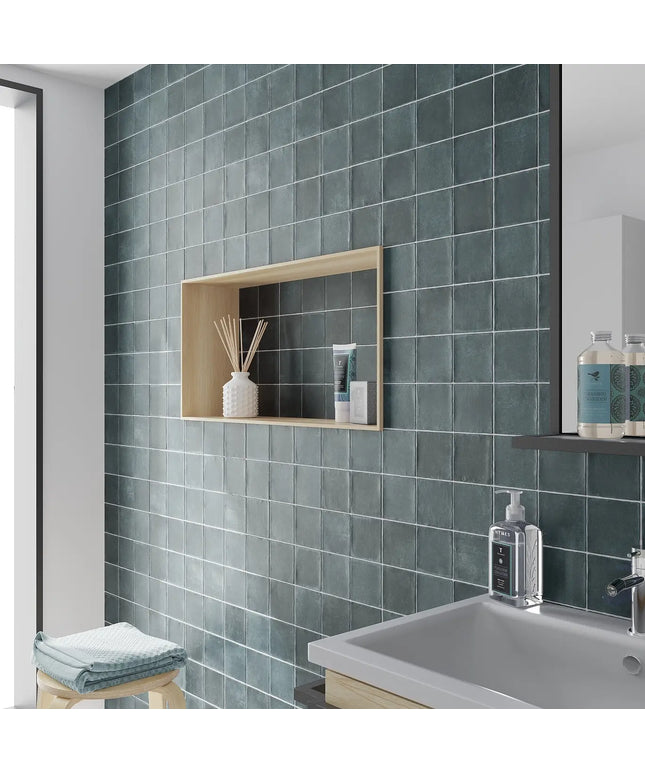 Bathroom with green tiled walls, a sink, and shelves with toiletries.