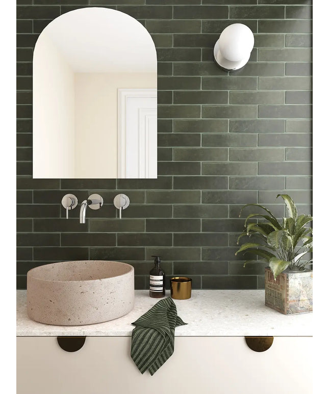 Bathroom with green tiled wall, white sink, and decorative elements.