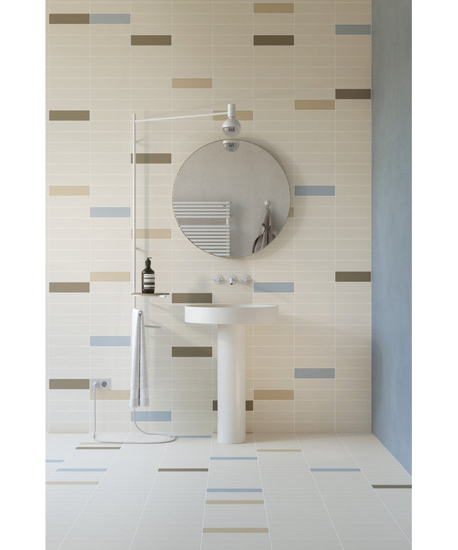 Modern bathroom with beige and colored rectangular wall tiles, pedestal sink, and round mirror