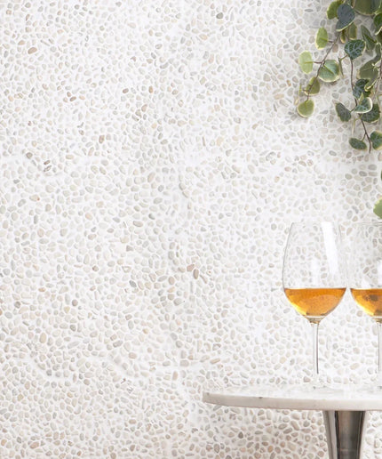 white stone wall tiles with pebble texture, marble table, two wine glasses, and green plant