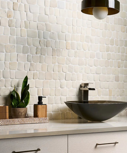 Modern bathroom vanity with a bowl-shaped sink, decorative items, and a tiled wall.