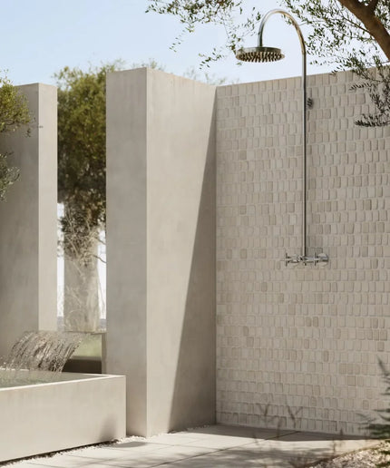 Outdoor shower with tiled wall and water feature, surrounded by trees.