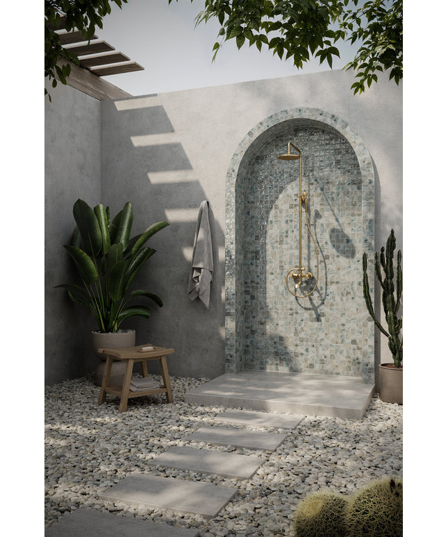 Outdoor shower area with stone walls, plants, and a wooden stool.