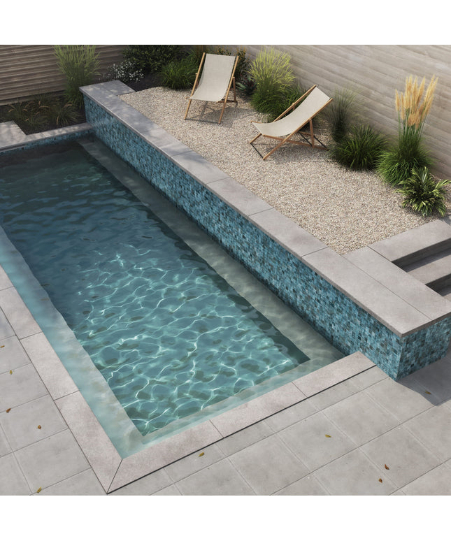 Small rectangular pool with pebble pavement and lounge chairs in a garden setting