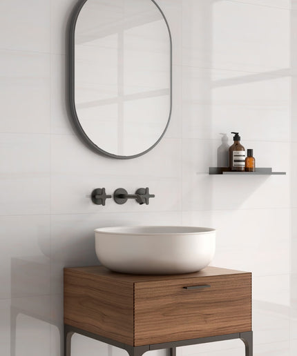 Bathroom vanity with wooden cabinet, white sink, and round mirror on a white wall.