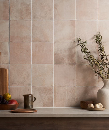 Beige tiles on a wall with kitchen items like a cutting board, pitcher, and fruit.