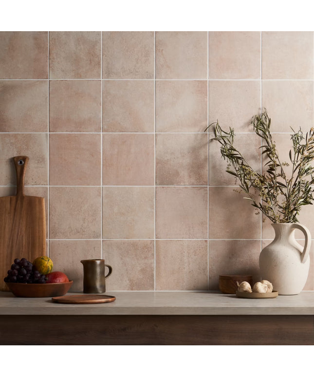 Beige tiles on a wall with kitchen items like a cutting board, pitcher, and fruit.