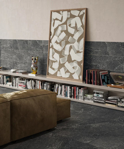 Living room with a bookshelf, brown ottoman, and abstract art on a gray marble floor.