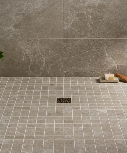 Tile floor with a shower drain and soap on a tray, against a tiled wall.