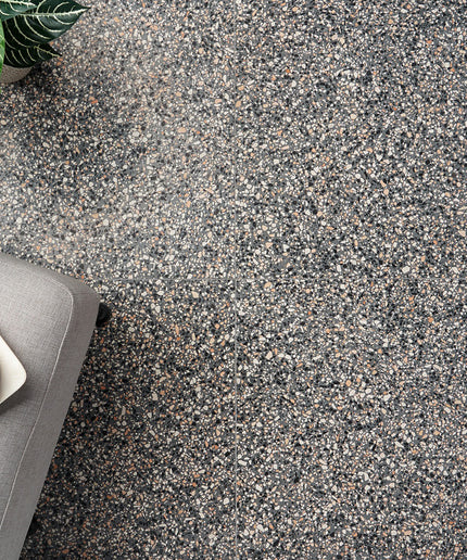 Close-up of a textured gray floor with a small plant and gray cushion in the corner.