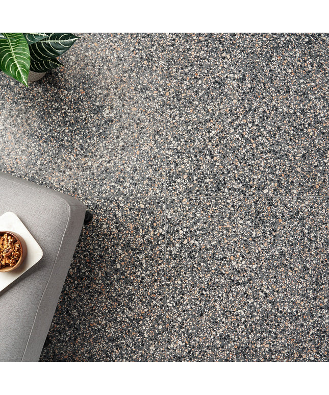 Close-up of a textured gray floor with a small plant and gray cushion in the corner.