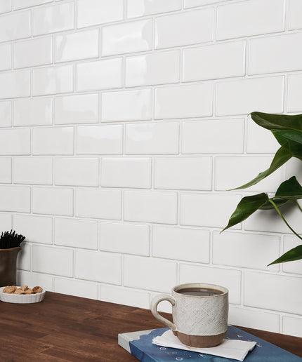 White tiled wall with a wooden table featuring a mug, plant, and small items.