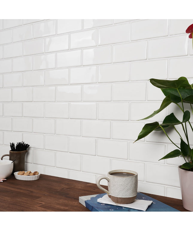 White tiled wall with a wooden table featuring a mug, plant, and small items.