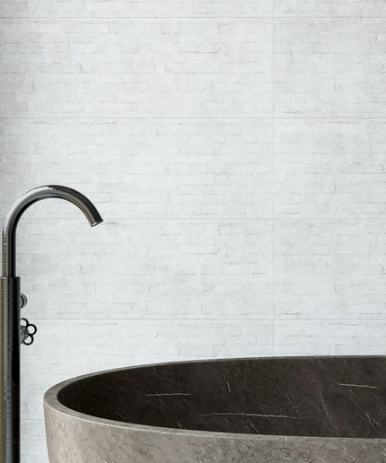 Light gray ceramic tile wall behind modern bathtub and faucet in bathroom setting