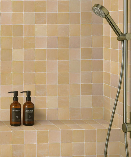 Bathroom shower setup with tiled wall, shower head, and bottles on a ledge.