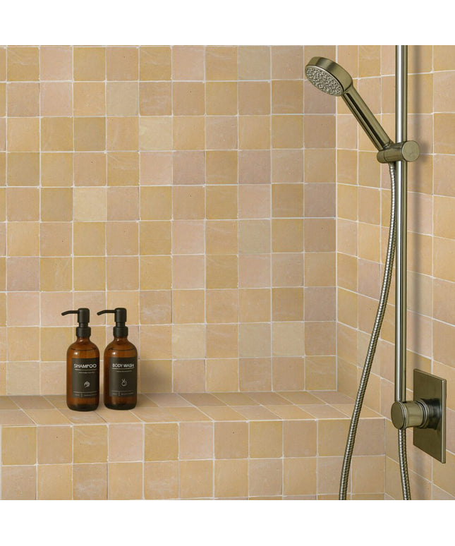 Beige zellige wall tiles in a shower with modern fixtures and two brown soap bottles.