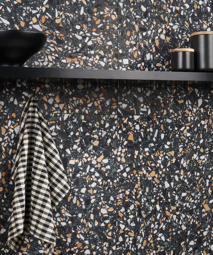 Terrazzo-patterned wall with black shelf, striped towel, and cylindrical objects.
