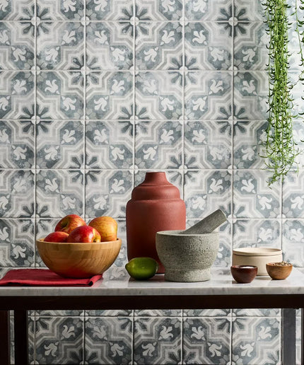 Decorative tiles with a floral pattern on a wall, featuring a table with a bowl of fruit and kitchen items.