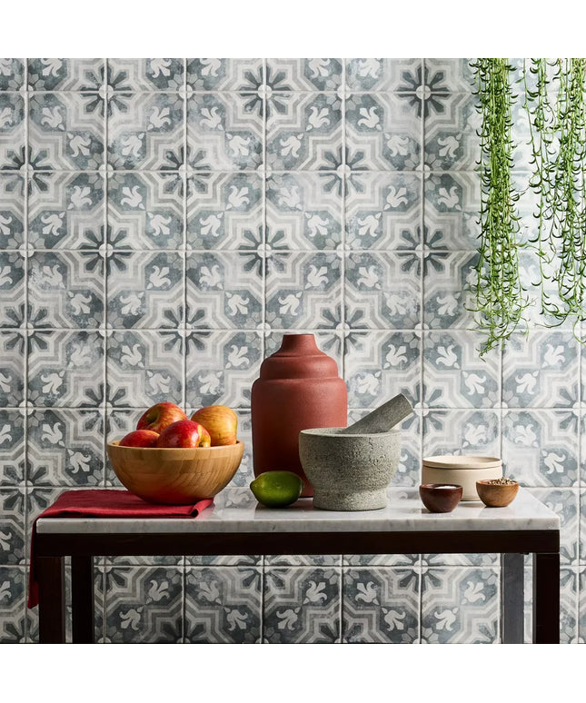 Decorative tiles with a floral pattern on a wall, featuring a table with a bowl of fruit and kitchen items.