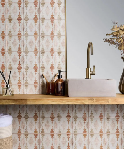 Bathroom counter with sink, faucet, and decorative items against a patterned wall.