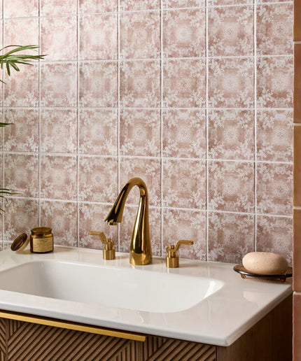 Bathroom sink with gold faucet against a patterned tile wall