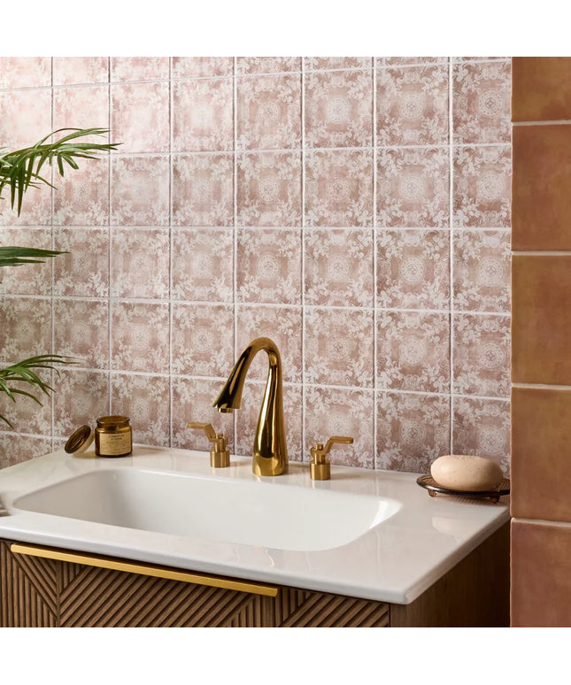 Bathroom sink with gold faucet against a patterned tile wall