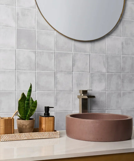 Bathroom setup with a round brown sink, mirror, and decorative items on a light gray tiled wall.