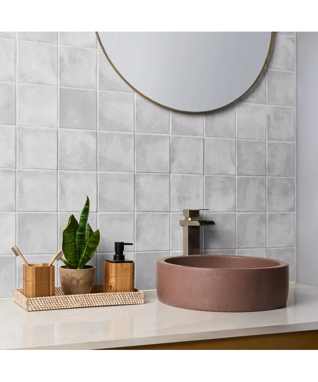 Bathroom setup with a round brown sink, mirror, and decorative items on a light gray tiled wall.