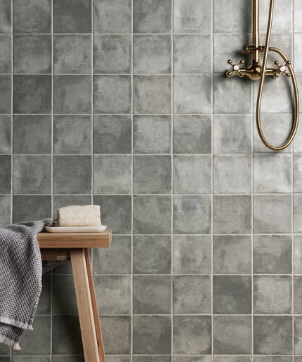 Gray tiled bathroom wall with a wooden stool and towel.