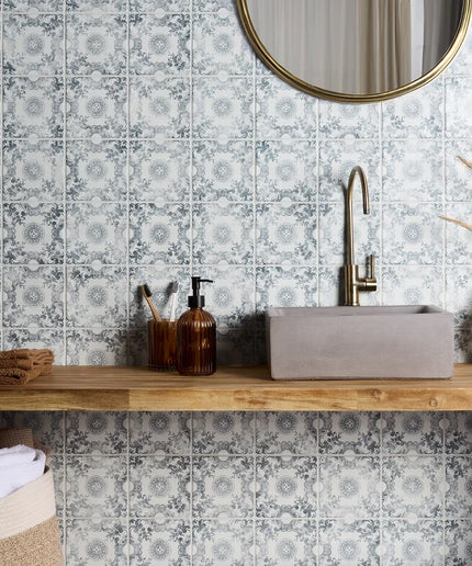 Bathroom with floral-patterned tiles, wooden vanity, and round mirror.