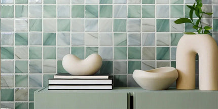 Decorative setting with ceramic bowls and books against a green tiled wall.