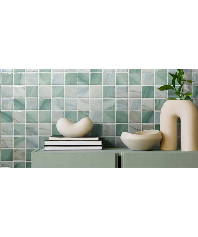 Glossy green and white mosaic wall tiles with decorative ceramic vases and books in front.