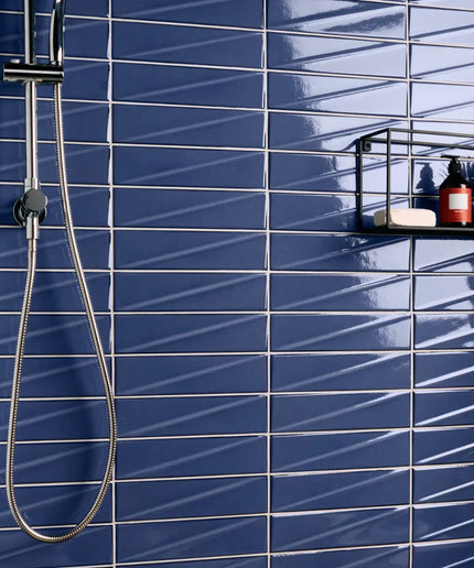 Shower setup against a blue tiled wall with a black shelf holding bottles and soap.