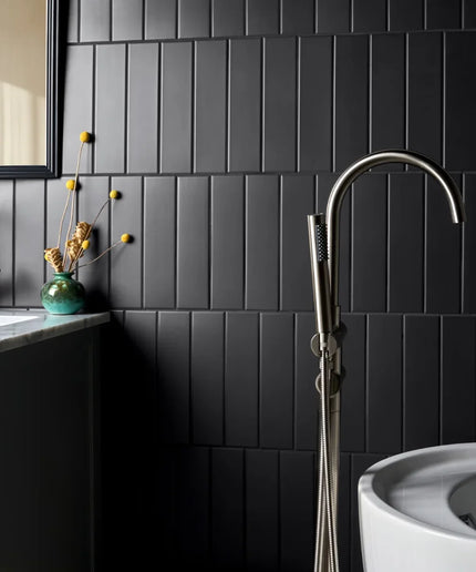 Modern bathroom with matte black 3x11 subway tile wall, freestanding tub, and sleek fixtures.