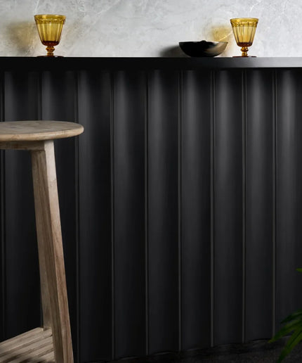 Black fluted column tiles 4x36 on wall, with wooden stool and decorative glasses